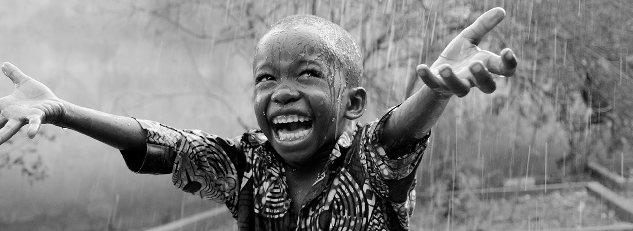 African child stretches his arms towards the sky in the rain.