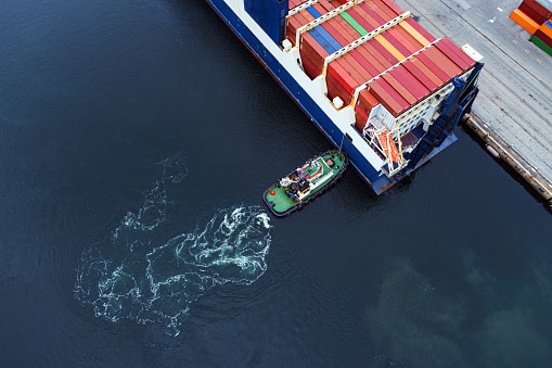 A container ship docks at port with the assistance of a tugboat.
